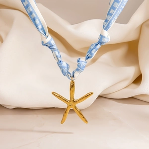 Primer plano detallado de un colgante de estrella de mar dorada en una cinta de seda azul y blanca