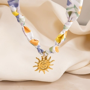 Primer plano de colgante de sol dorado con textura en espiral en collar de seda floral