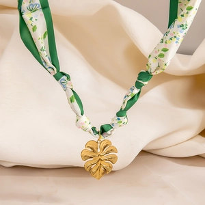Detalle del collar de pañuelo de seda verde con colgante de hoja de monstera oro