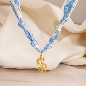 Detalle de collar de pañuelo de seda azul claro con colgante de coral dorado