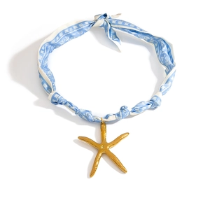 Detalle de collar de pañuelo de seda azul y blanco con un colgante de estrella de mar dorada