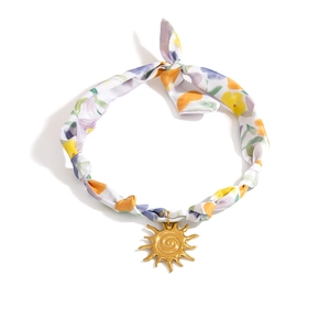 Detalle del collar bufanda de seda blanca con estampado floral y colgantes de sol dorado