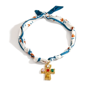 Detalle de collar tipo pañuelo de seda floral azul con colgante de cruz dorada