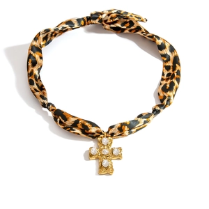 Close-up of hammered gold cross pendant with clear gems and leopard print silk cord necklace