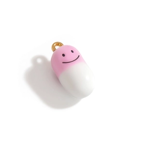 Détail d'un pendentif capsule rose et blanc avec un visage souriant noir et anneau doré