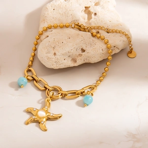 Golden stainless steel beaded chain bracelet with starfish charm and blue beads on a white rock