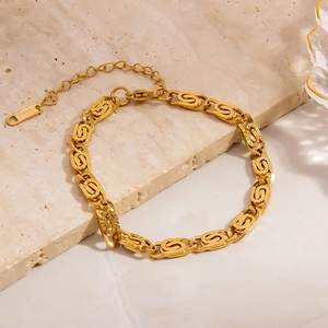 Bracelet chaîne irrégulier en acier doré texturé posé sur une surface en marbre beige