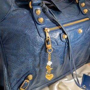 Détail d'un sac en cuir bleu foncé à effet craquelé avec clous dorés et breloques colorées