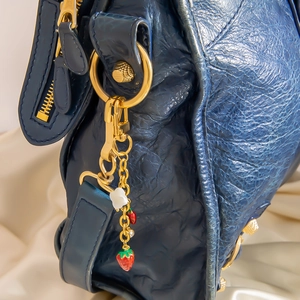 Détail du sac de moto en cuir bleu avec ferrures dorées et breloques pendantes de fraises