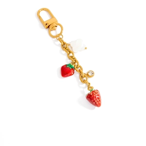 Détail d'un porte-clés doré 18 carats avec breloques fraise en émail et fleur blanche