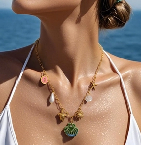 Detail of 18K gold-plated necklace with sea shell, turtle, and sun charms on ocean background