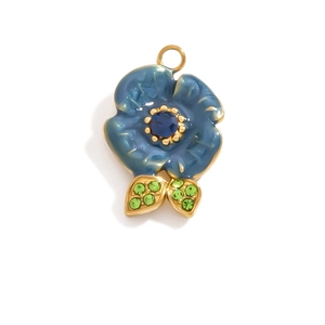 Detailed macro view of 18K gold-plated flower pendant with blue enamel and green gems