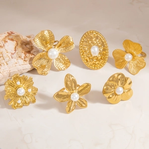 Detail showing gold flower rings with pearls on beige marble background with shell