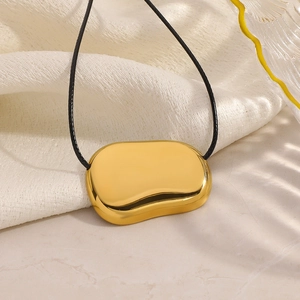 Close-up of a polished gold bean pendant on a black cord with textured fabric background