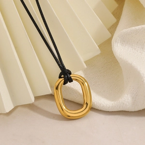 Detail view of a minimalist golden irregular oval pendant on a black cord necklace