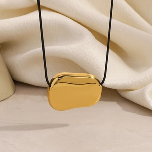 Minimalist gold irregular pebble pendant necklace with sleek black cord on beige fabric