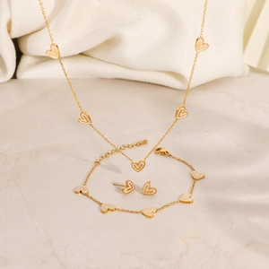 Golden stainless steel heart jewelry set with necklace, bracelet and earrings on marble