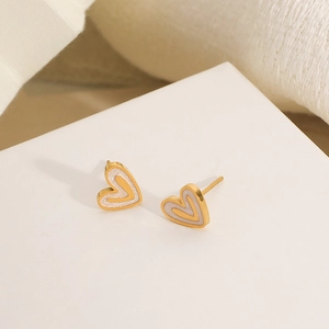 Close-up of golden heart stud earrings with white glitter inlay and small inner heart