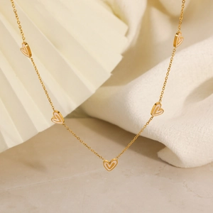 Detail of 18K gold heart charms with white inlay on a dainty necklace chain