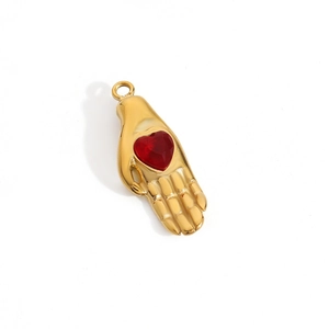 Detail of 14K gold plated hand holding a red heart pendant with a polished finish