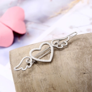 Silver heart-shaped hair clip with delicate feather wings on a minimalist stone display
