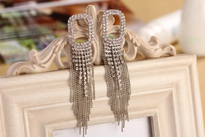 Dettaglio di orecchini pendenti con strass argentati appesi a una cornice bianca vintage