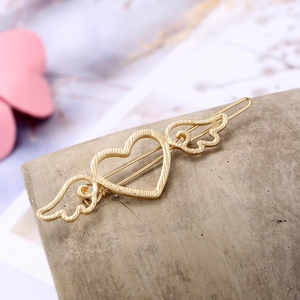 Elegant gold bow hair clip with textured heart wings on a stylish concrete display stand
