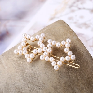 Eleganter goldener Haarclip mit zwei verbundenen Sternen und weißen Perlen auf Stein