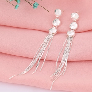 Boucles d'oreilles pendantes à pompons argentés sur fond de tissu rose doux