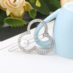 Detail of silver clover hair clip with rhinestones and pearl resting on a cup