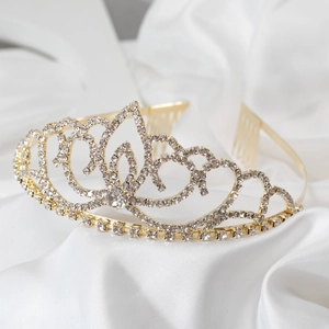 Detailed side view of golden rhinestone tiara with side hair combs on white satin fabric