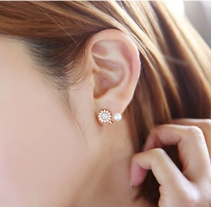 Détail de boucles d'oreilles tournesol et perle rose doré portées sur modèle