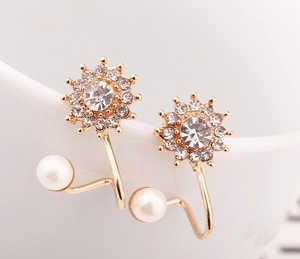 Vue macro d'une boucle d'oreille fleur avec strass et perle blanche sur porcelaine blanche