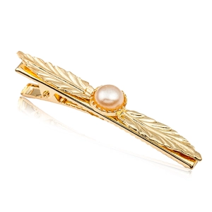 Elegant gold leaf hair clip with a centered round pearl on a reflective white surface