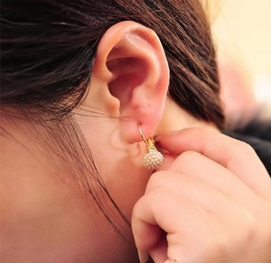 Detail eines eleganten Goldhaken-Ohrrings mit runder weißer Micro-Perlen-Cluster-Kugel