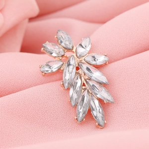 Detailed view of leaf-shaped rose gold brooch with marquise-cut crystals on pink fabric