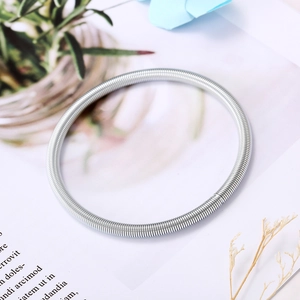 Bracelet jonc à ressort en acier inoxydable argenté posé sur un fond de magazine esthétique