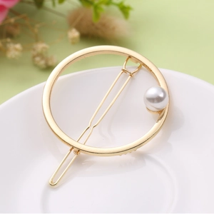 Barrette à cheveux dorée ronde et minimaliste avec une perle blanche sur un plateau élégant