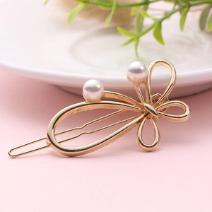 Elegant gold bow hair clip with white pearls on a minimalist pink and white background