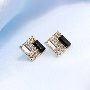 Detail of square stud earrings with black and white gems on blue silk fabric
