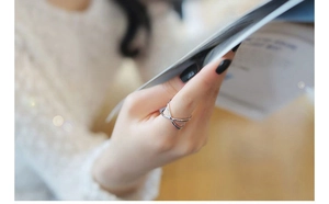 Close-up of a minimalist silver criss-cross X ring worn on a finger in a natural setting