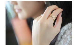 Close-up of a gold X-shaped cross ring with a small zircon accent on a model finger