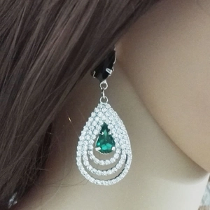 Détail de boucles d'oreilles goutte avec une gemme poire verte et cristaux blancs