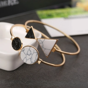 Dettaglio di bracciali dorati aperti con inserti in pietra marmorizzata tondi e triangolo