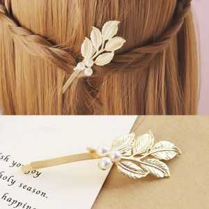 Détail d'une pince à cheveux feuille dorée avec perles blanches et texture élégante