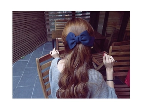 Détail d'une grande pince à cheveux nœud en tissu bleu marine sur une coiffure mi-haute
