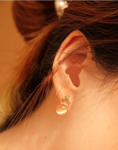 Close-up of model wearing an elegant gold crown earring with a warm orange cat eye stone