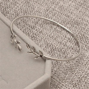 Detailed macro view of silver olive leaf open cuff bracelet on grey velvet stand