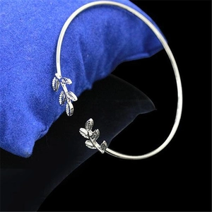 Detail view of silver open leaf cuff bracelet on a blue cushion with polished finish