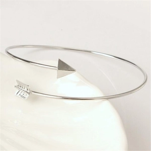 Polished silver arrow open bangle with arrowhead and feather design on white textured tray